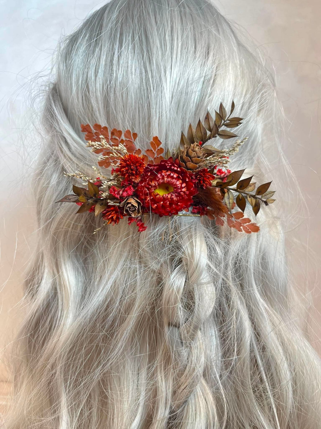 Hair comb crafted entirely from preserved and dried botanicals in deep, rich autumn tones - vivid crimson strawflowers, velvety dried roses, rustic pine cones, warm brown leaves, and delicate dried grasses.