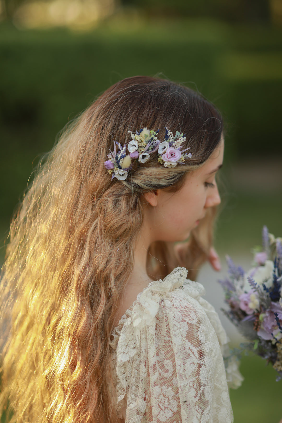 Woman with floral purple and cream hairpins and bouquet in a natural setting