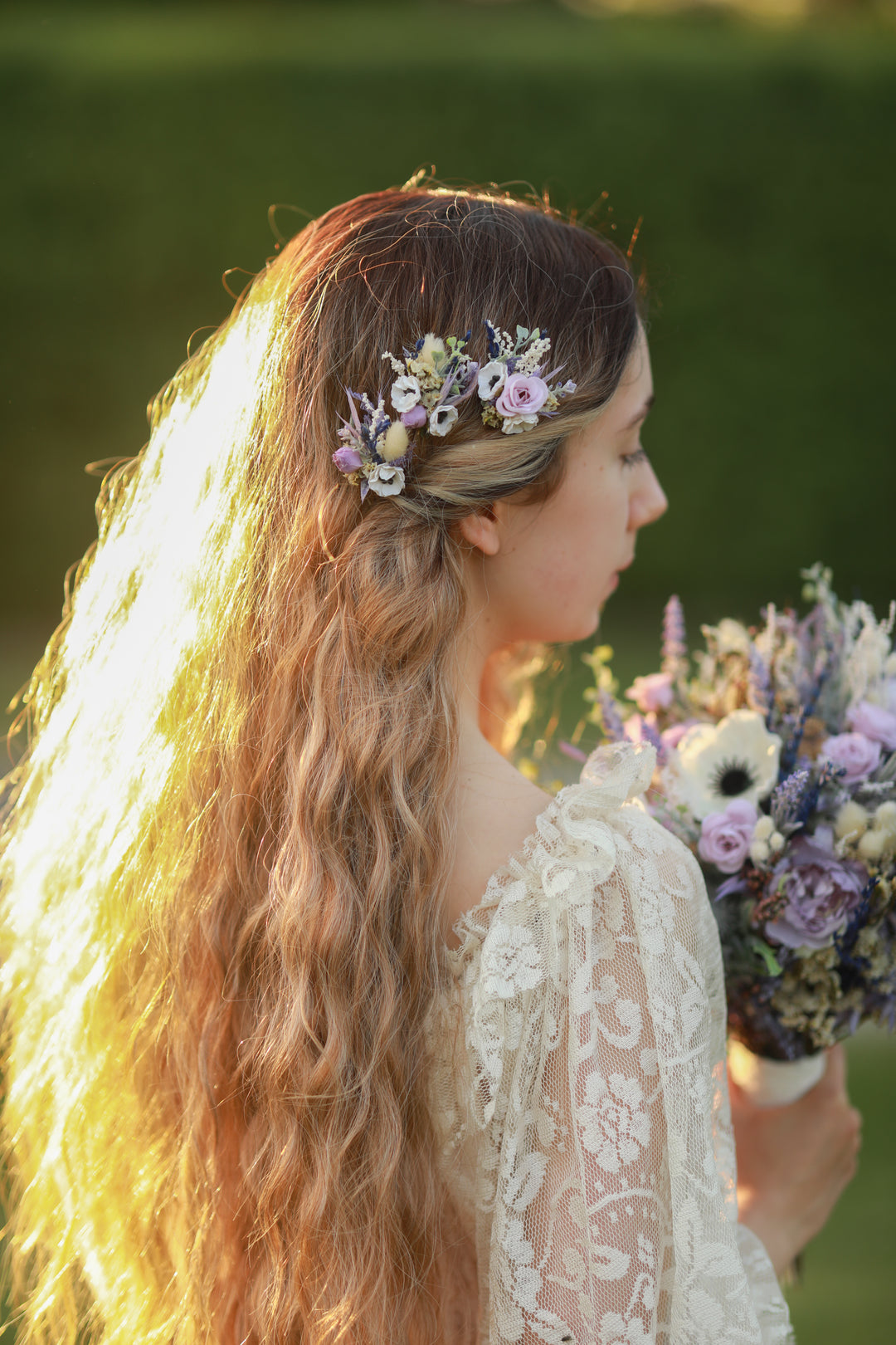 Woman in a lace dress with a floral hairpins n rustic style and bouquet, standing outdoors.