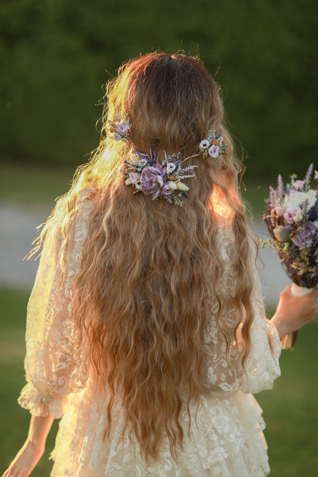 Woman with long hair and floral hair accessories holding a bouquet outdoors.