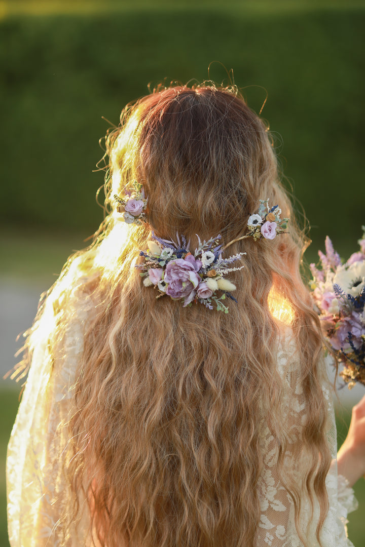 Woman with long, wavy hair adorned with floral hair accessories and a bouquet, standing outdoors.