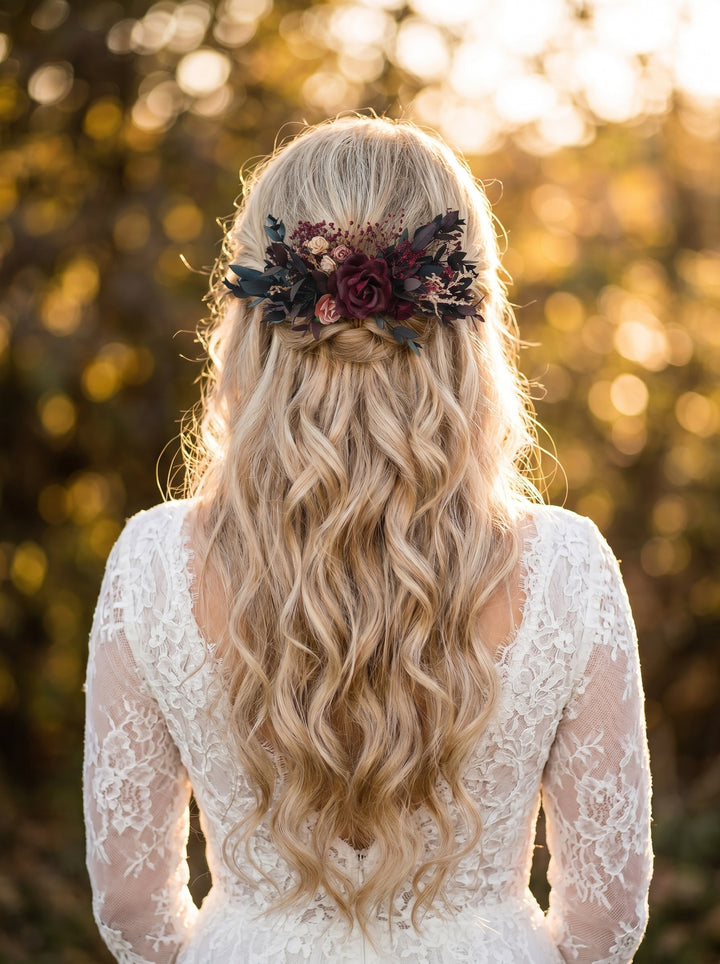 Bride with long blonde hair wearing a floral burgundy rustic hair comb, standing outdoors with a blurred natural background.