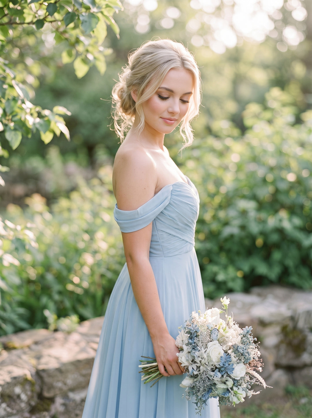 A woman outdoors in a light blue off-the-shoulder midi dress holding a bouquet of white and blue flowers, with a blurred garden background.