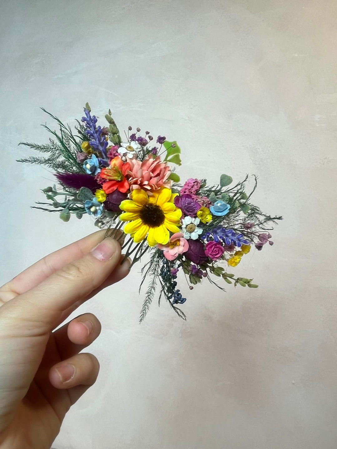 Colorful flower hair comb held by a hand against a plain background