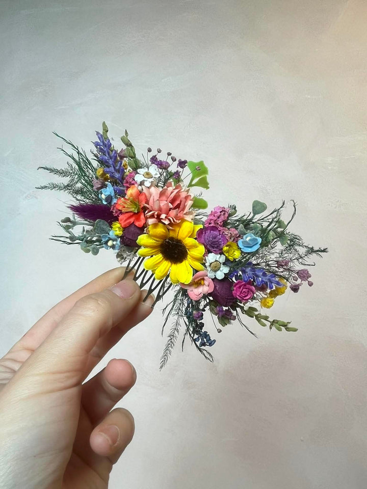 Colorful floral hair comb held by a hand against a plain background