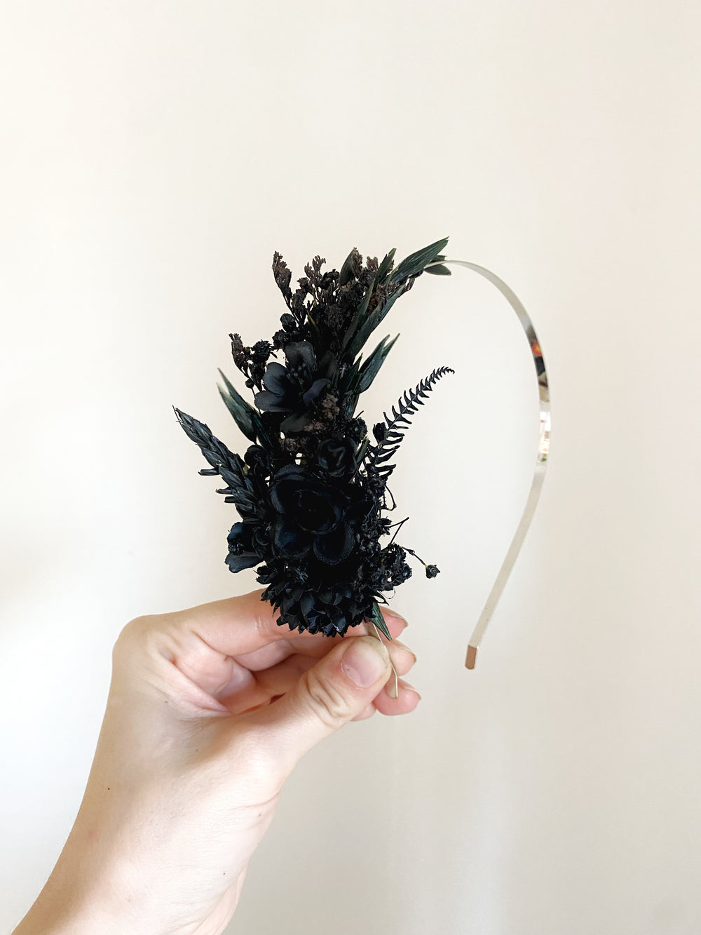 A hand holding a black floral headband with a curved clear plastic band against a plain off-white background.