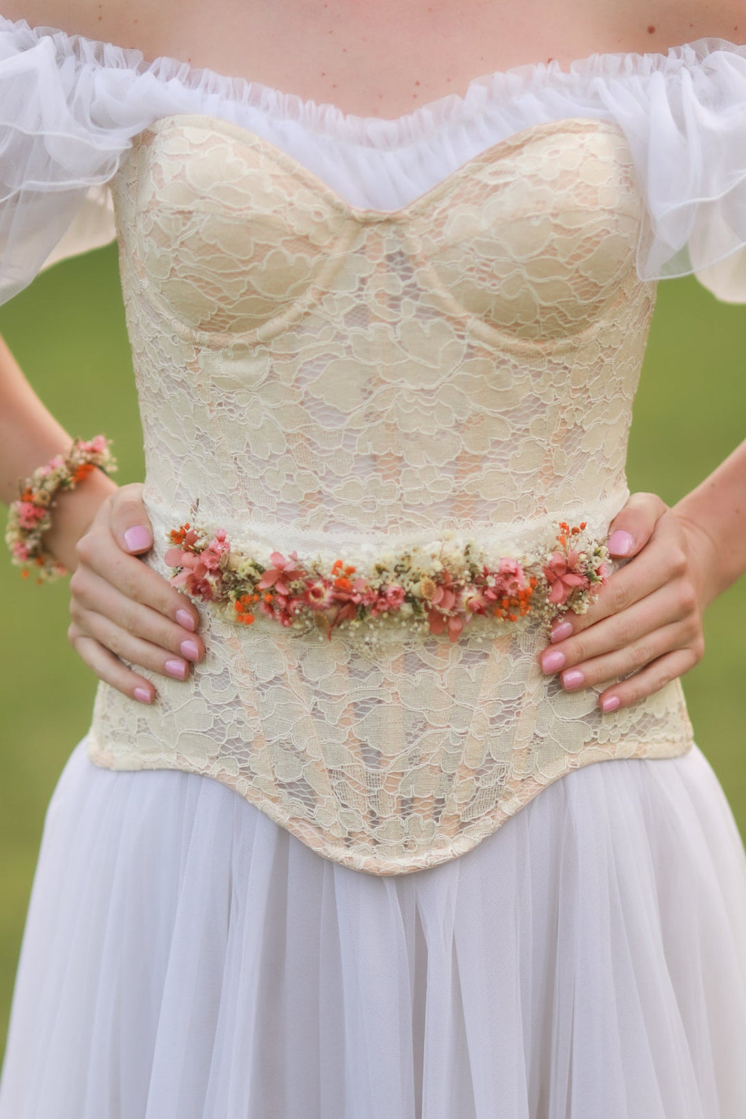 Lace corset with floral belt worn by a person against a blurred green background