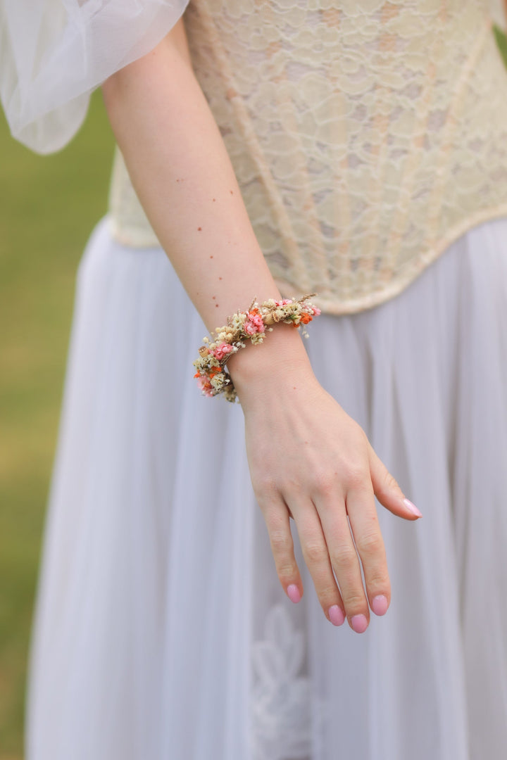 Person wearing a lace top and light skirt with a colorful bracelet from dried flowers, outdoors.