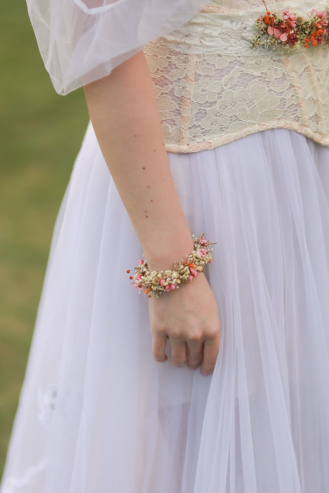 Person wearing a floral bracelet from dried flowers in pink, orange and cream tones  with a blurred natural background