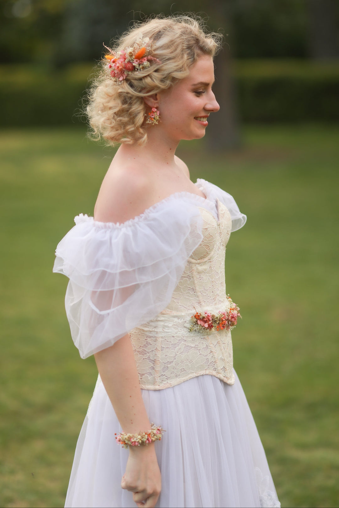 Woman in a white dress with floral accents standing outdoors on a grassy area.