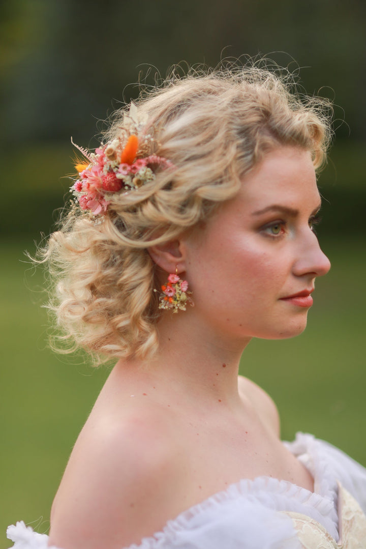 Woman with styled hair featuring flowers, wearing a white dress against a blurred green background