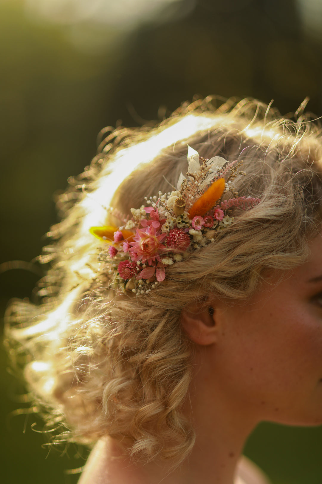 Close-up of a person with floral dried meadow pink and orange hair comb against a blurred natural background