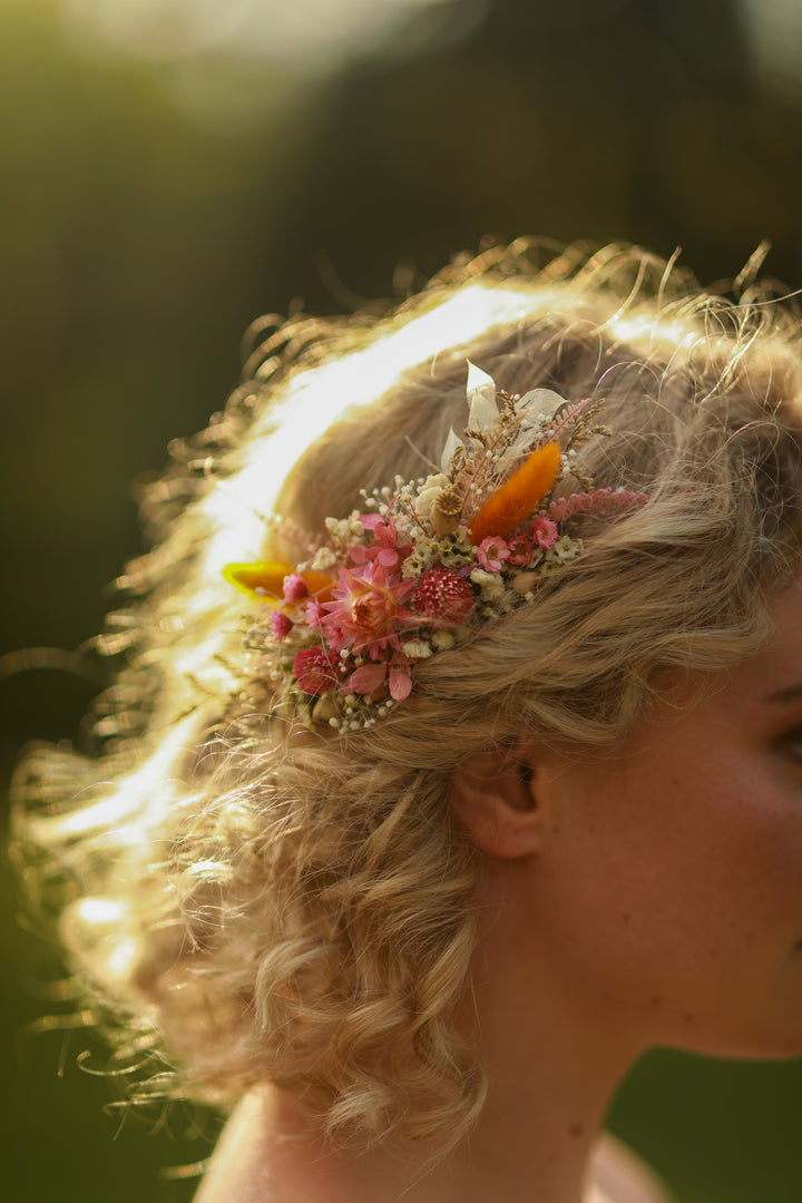 Close-up of a person with floral dried meadow pink and orange hair comb against a blurred natural background