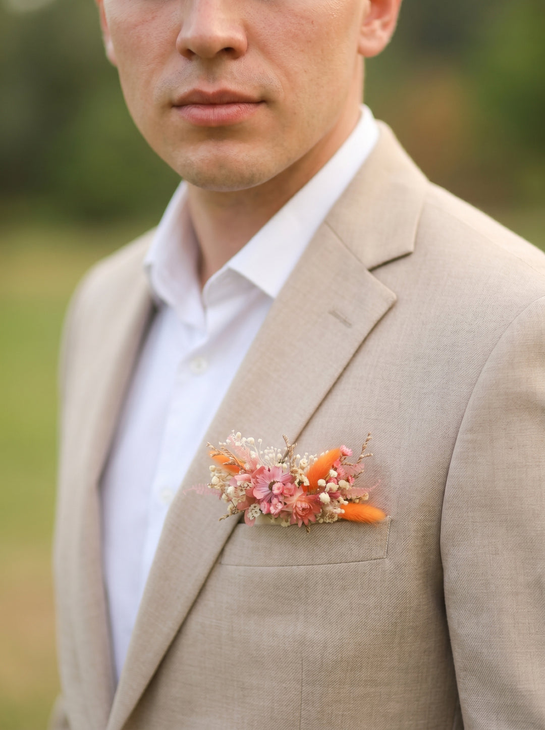 Man wearing a beige suit with a colorful boutonniere outdoors