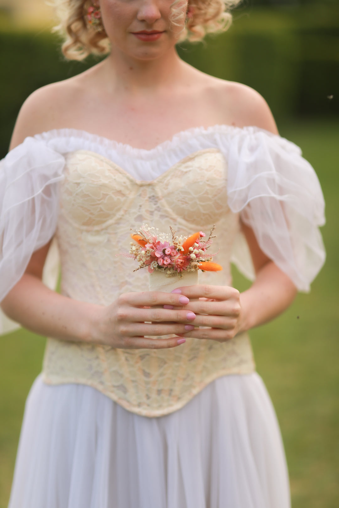 Woman wearing a floral corset top with a white skirt against a blurred green background