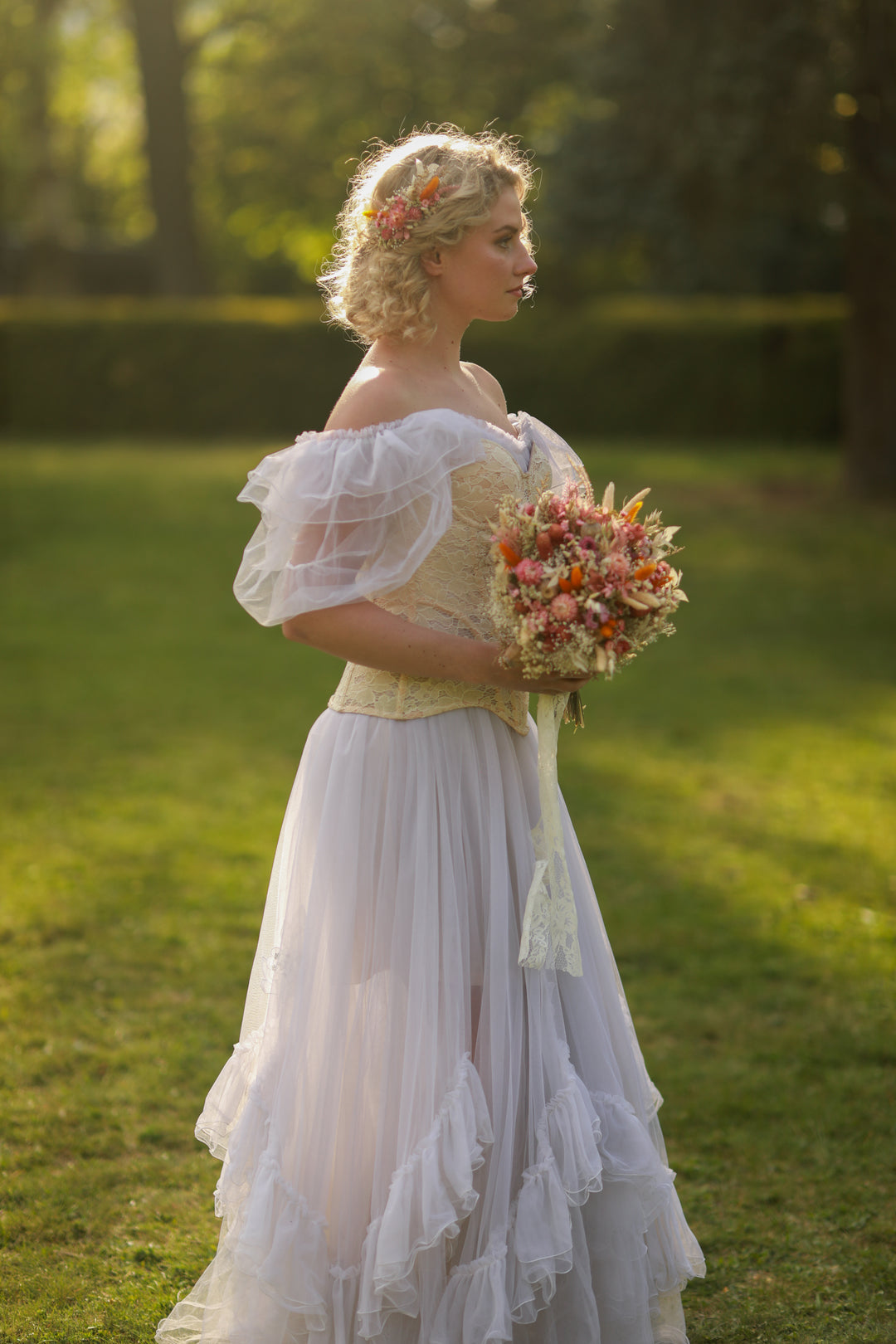 Woman in a vintage-style dress holding a bouquet of flowers in a park.