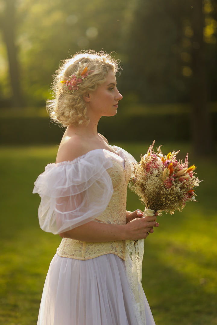 Woman in a historical dress holding a bouquet of dried and preserved  flowers in a park setting
