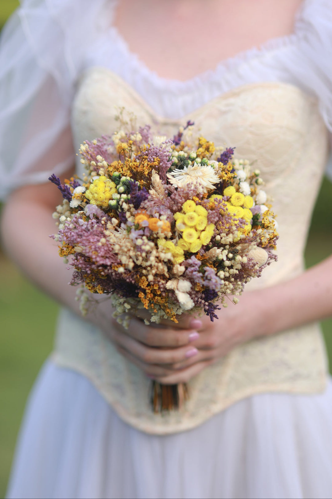 Person holding a bouquet of dried flowers with a blurred background