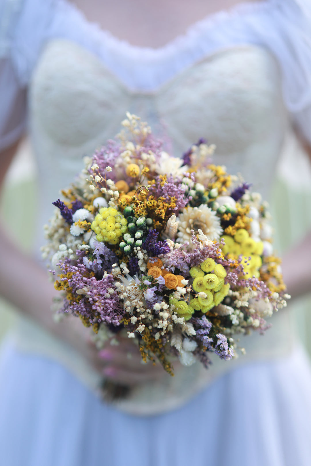 Bouquet of dried wild flowers held by a person wearing a light-colored dress.