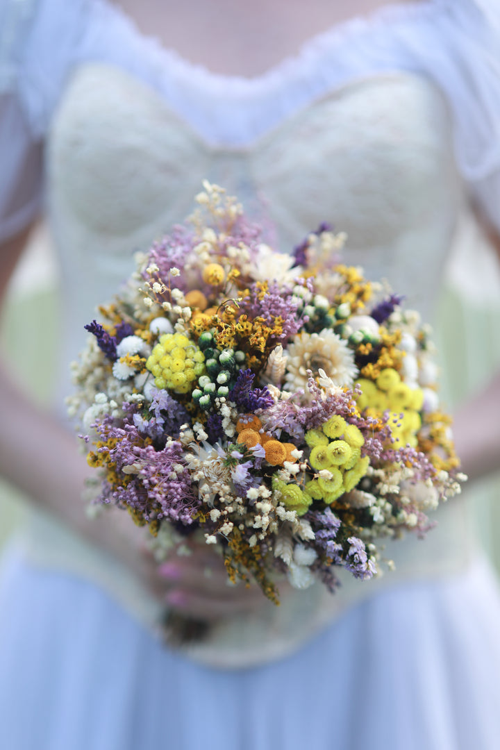Bouquet of dried wild flowers held by a person wearing a light-colored dress.