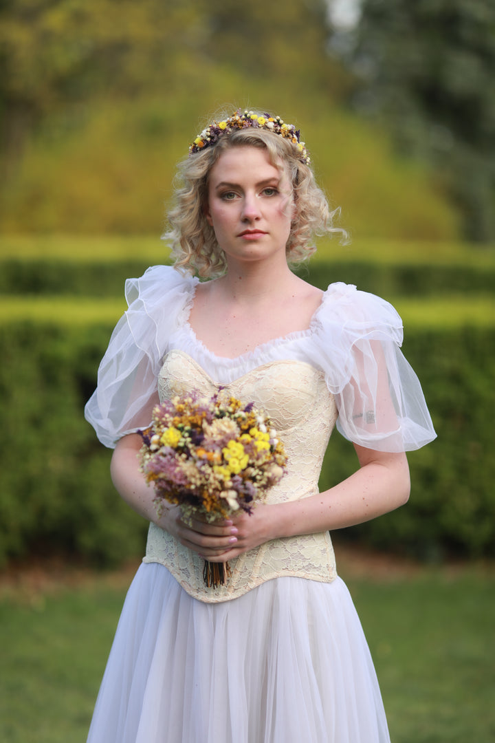 Woman in a vintage-style dress holding a bouquet of dried flowers outdoors.