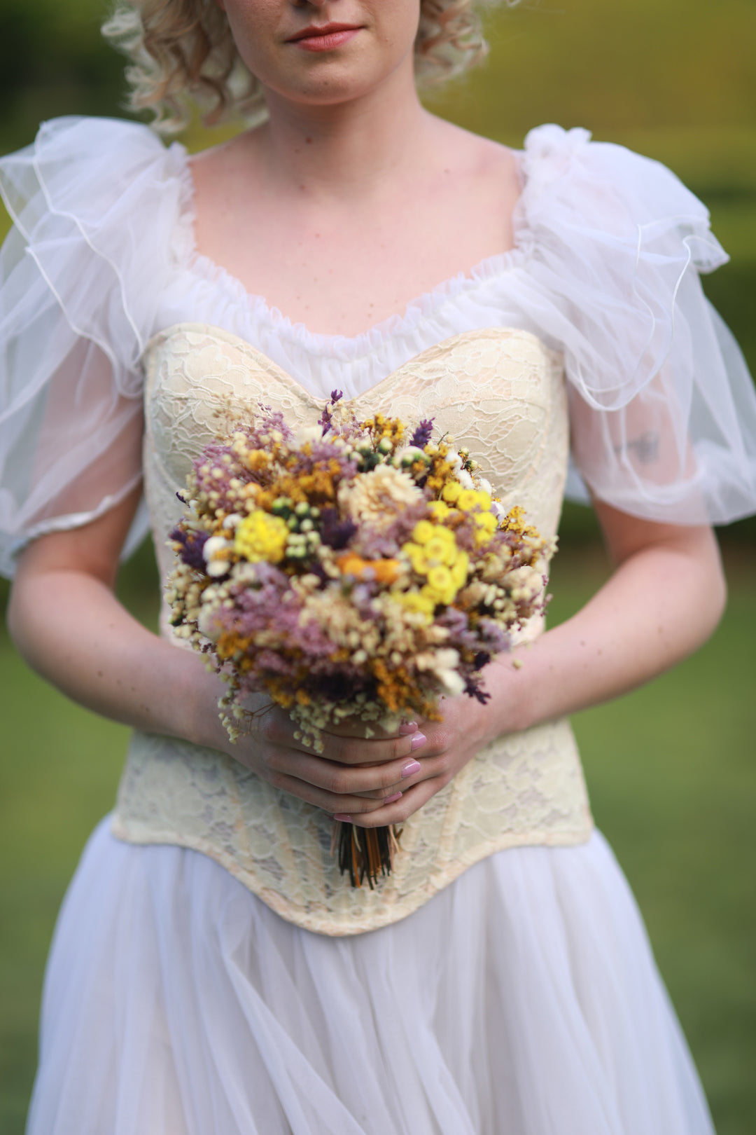 Woman in a white dress holding a bouquet of colorful meadow flowers against a blurred green background