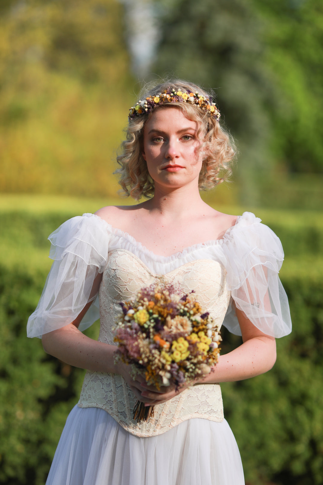 Woman in a vintage-style dress holding a bouquet of flowers outdoors.