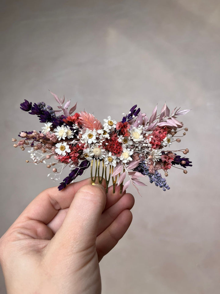 Hand holding a floral hair comb from preserved and dried flowers against a neutral background