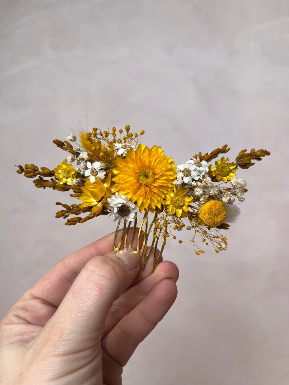 Hand holding a floral hair comb with yellow and white flowers against a plain background