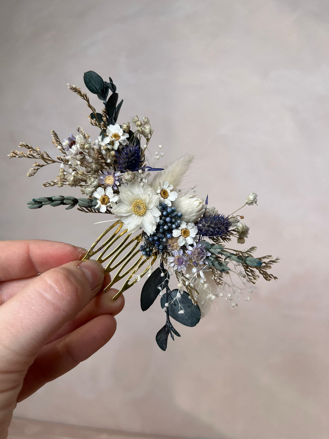 Floral hair comb from dried flowers  held by a hand against a plain background