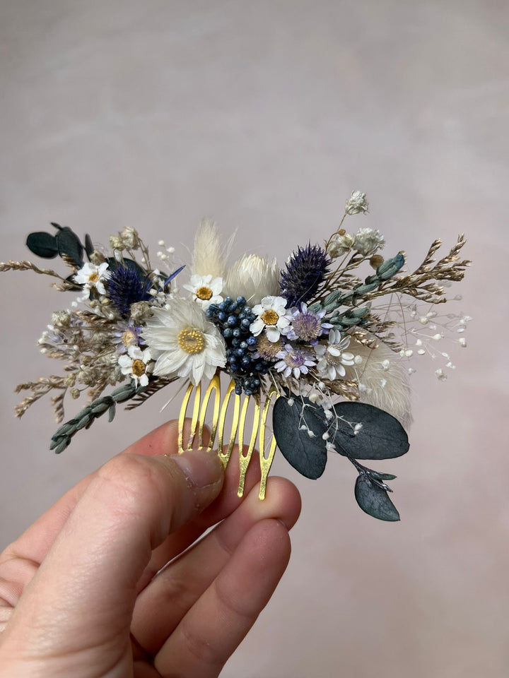 Hair comb with dried flowers and leaves held by a hand against a neutral background