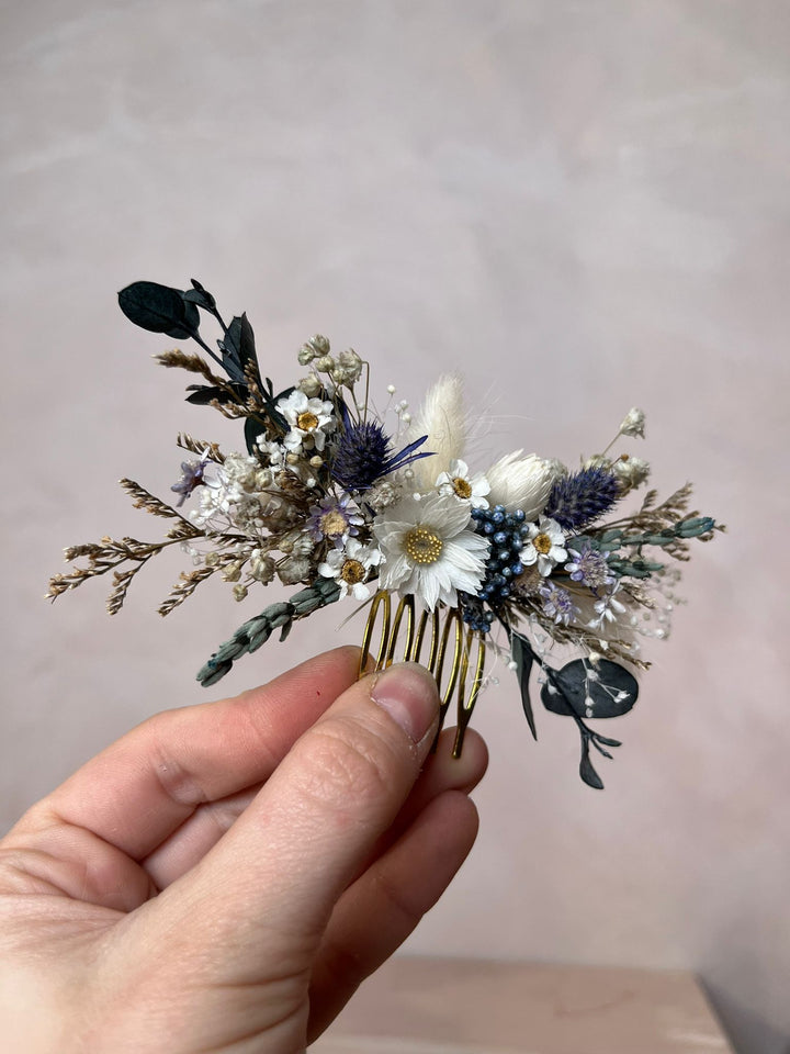 Hand holding a decorative hair comb with flowers and leaves against a plain background