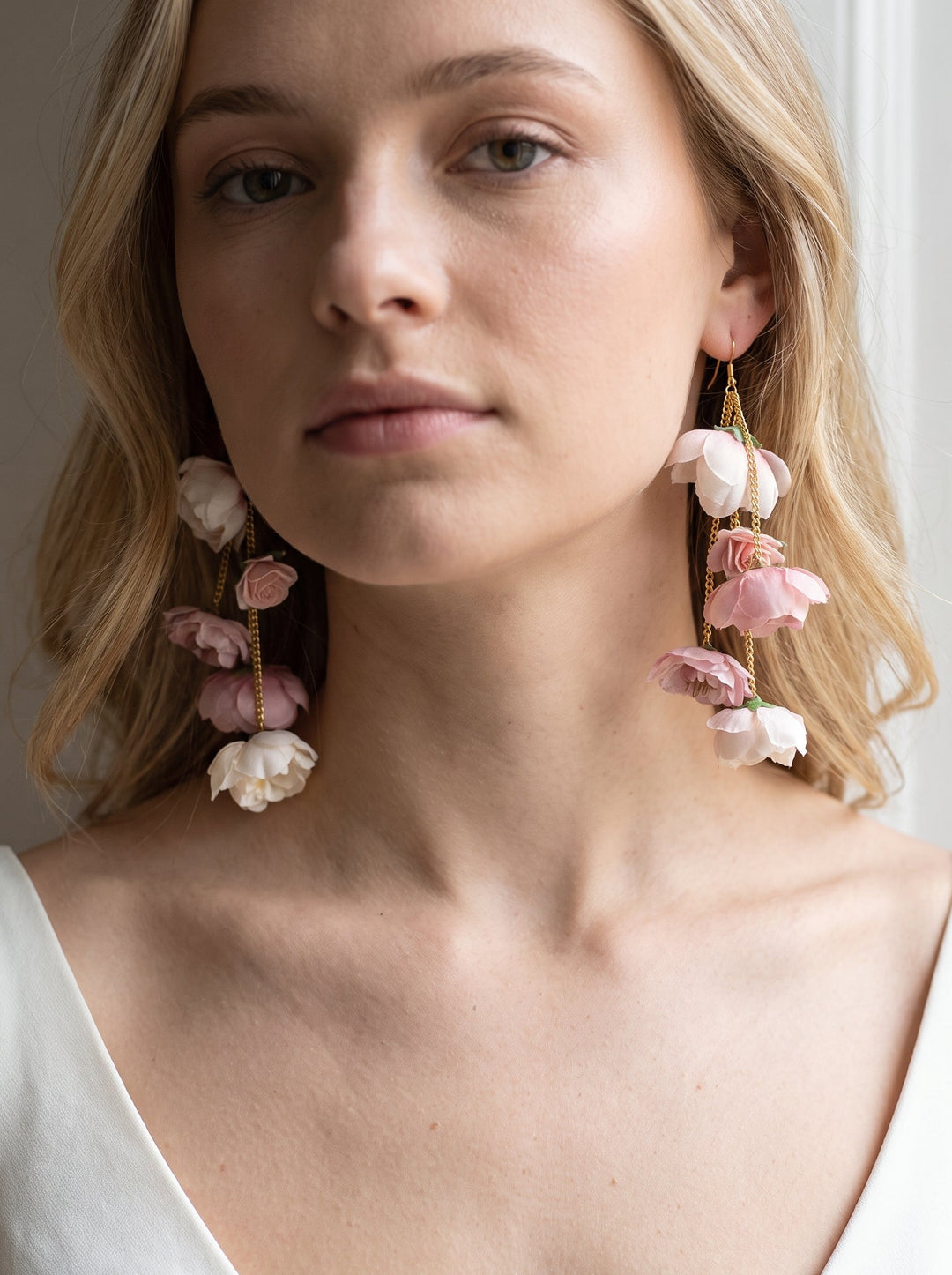 A close-up of a woman wearing large floral drop earrings with pink and white flower charms hanging from gold-toned hooks.