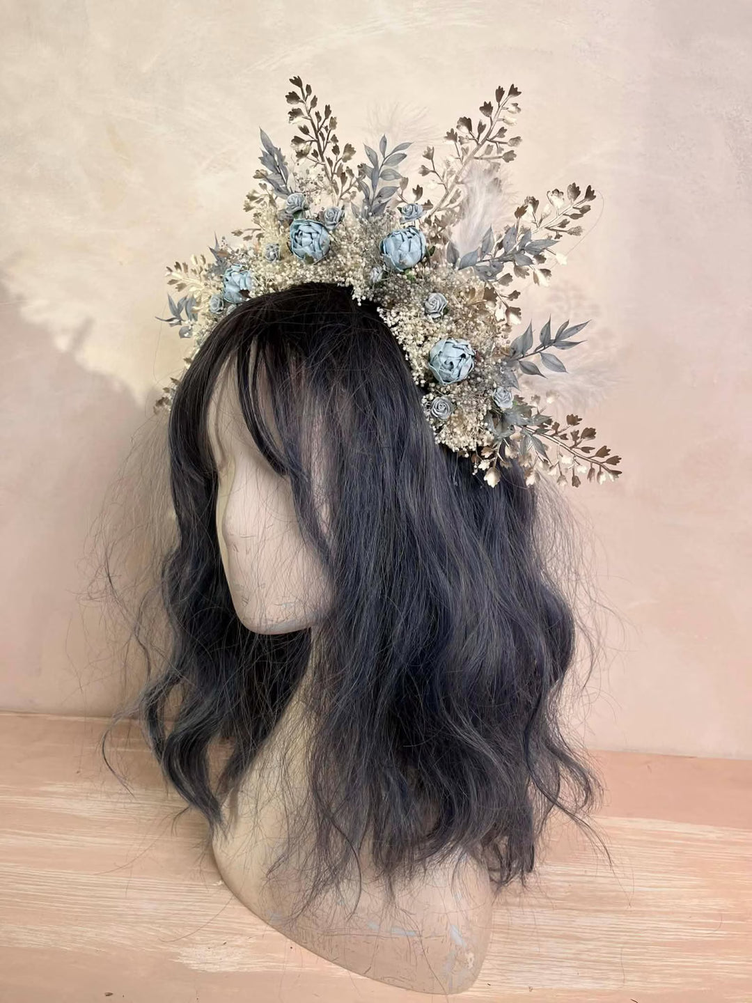 Floral headpiece in dusty blue tones  on a mannequin head with dark hair against a neutral background