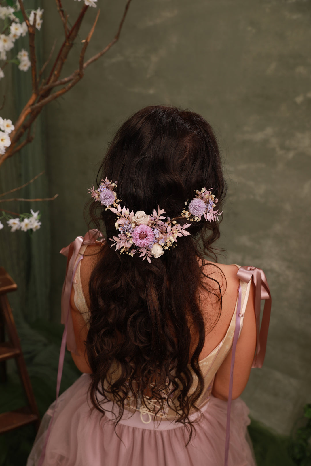 Person with floral hair accessory and pink dress against a green background