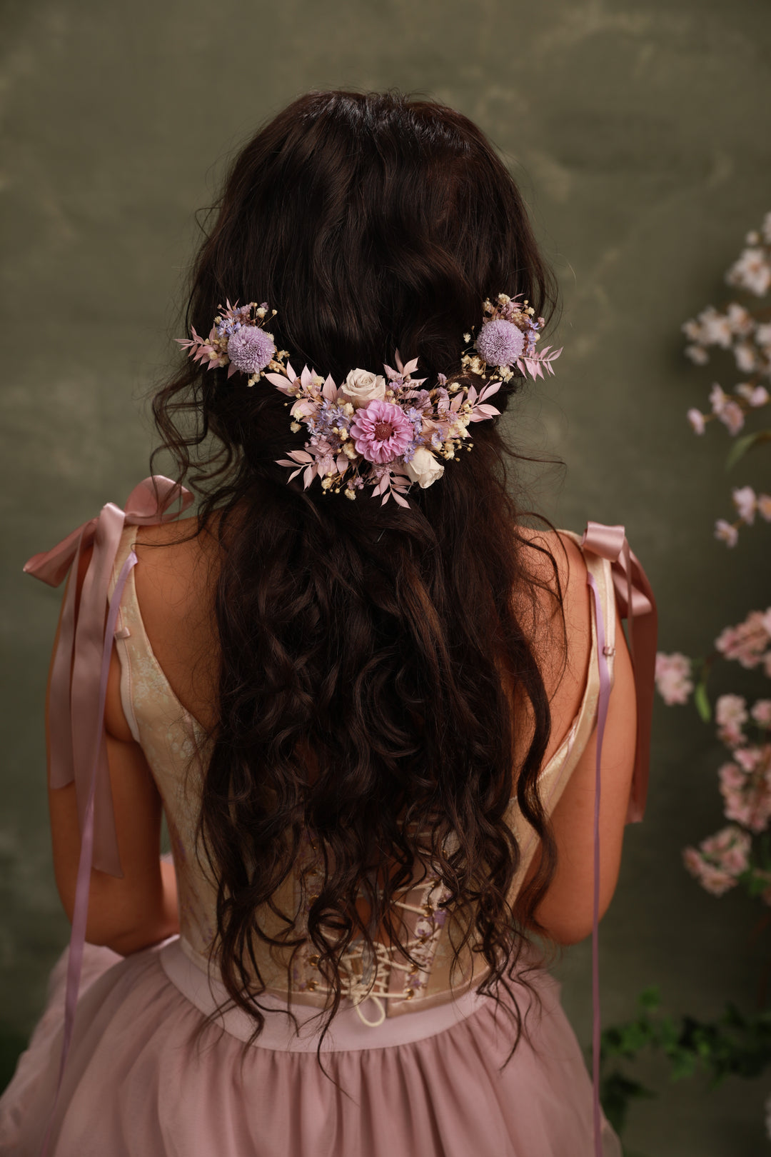 Woman with floral hairpiece from preserved flowers in purple tones  and pink dress against a green background