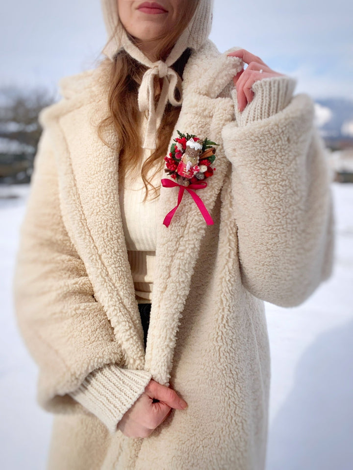  Woman in beige teddy coat in winter time with limited edition handmade Nutcracker Christmas brooch with red berries, pine cones, cinnamon and a bow for coats, hats and scarves