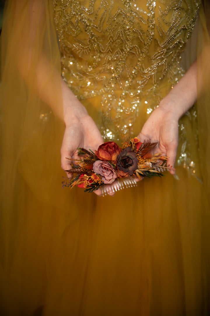 A close-up of a person wearing a shimmering beaded dress and holding a small floral hair accessory with textile and  dried autumn flowers 