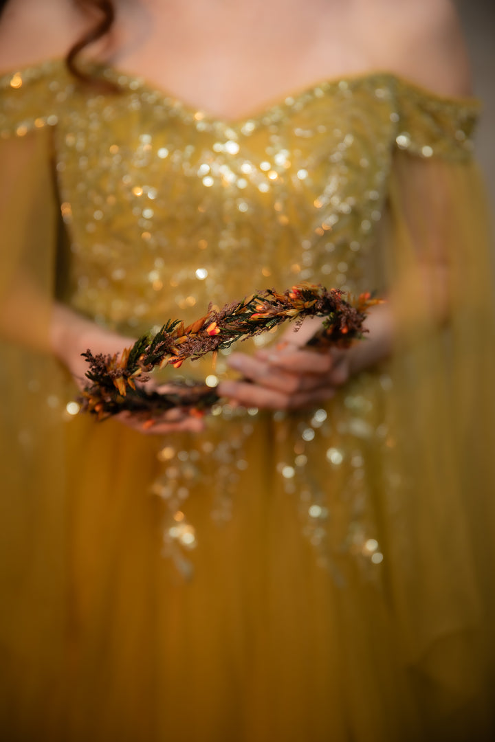 A close-up lifestyle shot of a person wearing a sparkling sequined gown and holding a decorative autumn wreath with orange berries.