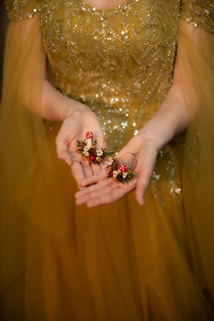 A close-up of a person wearing a shimmering gold sequined dress, holding two circle earrings in their hands against a dark background.