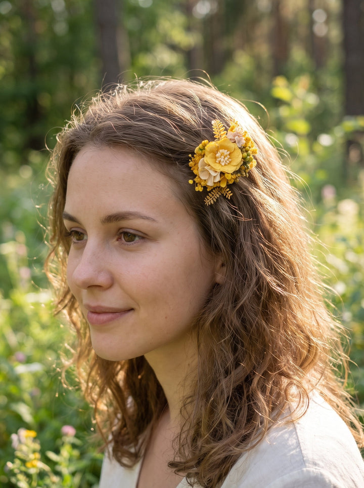 A woman with wavy brown hair wearing a yellow floral hair clip, photographed outdoors in a sunlit forest clearing.