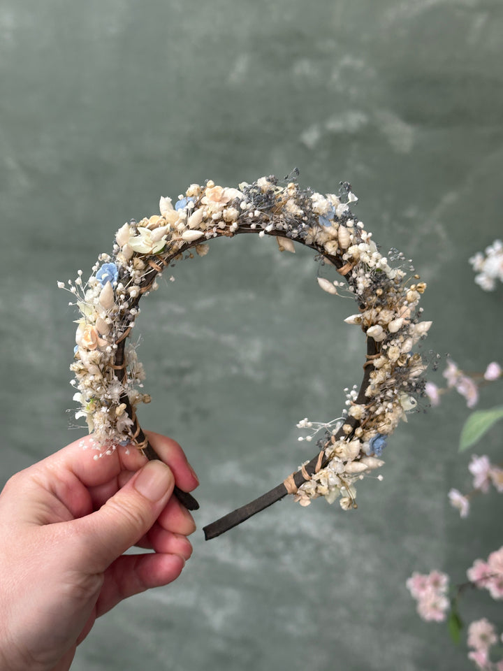 A handmade circular headband decorated with flowers held by a hand against a textured gray background.