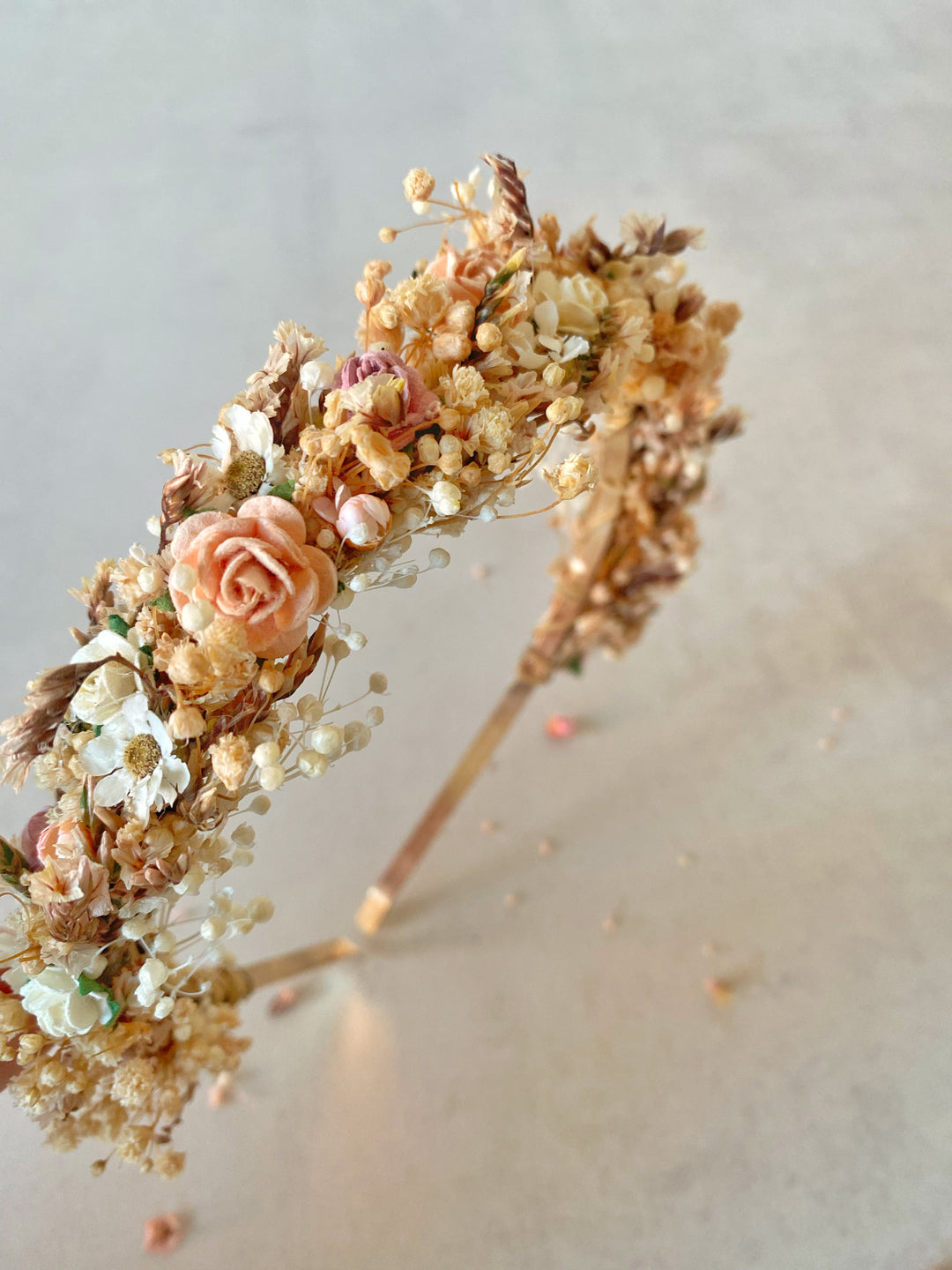 A floral headband featuring peach roses, baby's breath, and other delicate botanicals, displayed on a neutral light gray background.