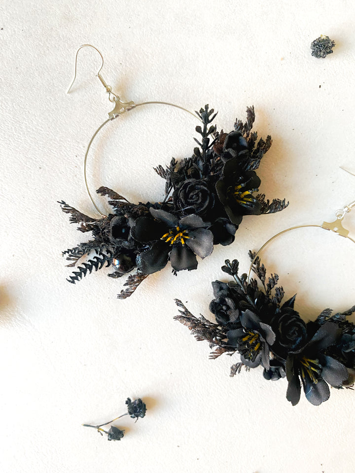Black flower hoop earrings with silver-toned wire frames, displayed on a textured off-white background.