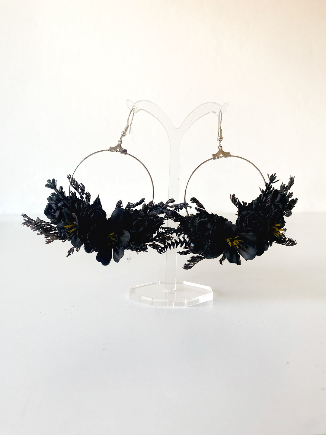 Black floral hoop earrings with silver-tone wire hoops and gold-toned hooks, displayed on a clear acrylic stand against a white background.