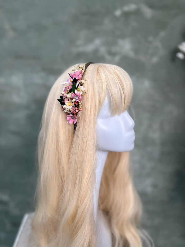 A long blonde wig displayed on a white mannequin head, styled with a floral headband featuring pink, white, and yellow flowers with green leaves.