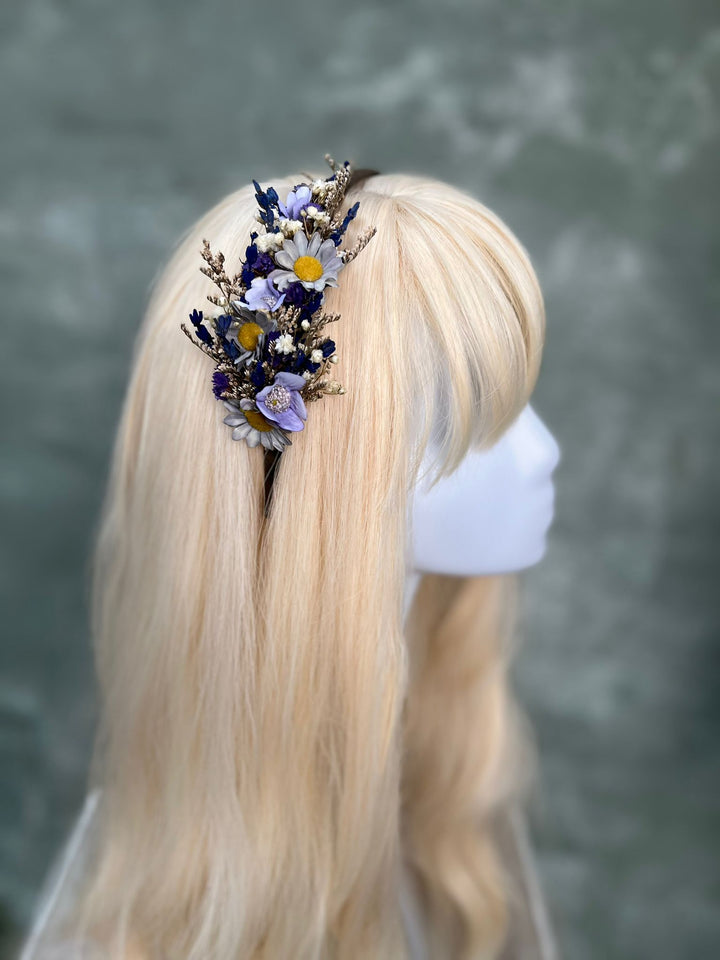 A blonde mannequin head wearing a cluster of dried flowers in a hair accessory, shown from the back against a soft gray background.