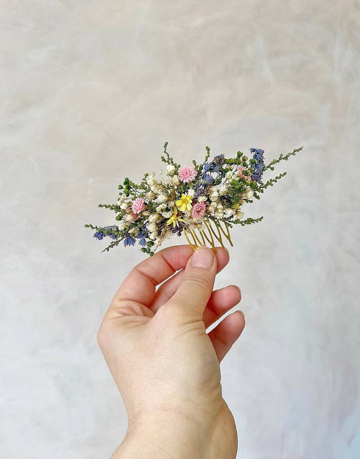 Hand holding a hair comb with dried flowers against a neutral background