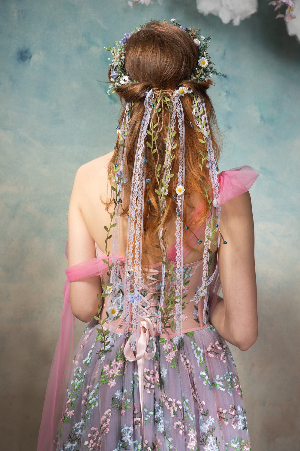 Woman in a floral dress with decorative hair accessories against a textured wall.