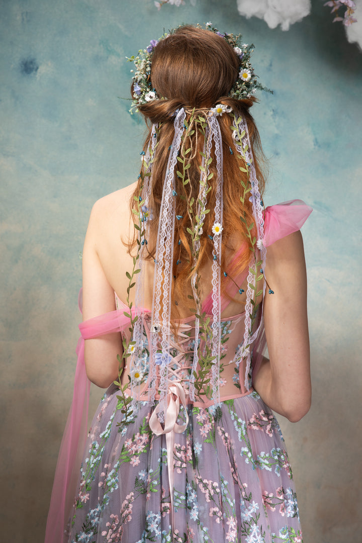 Woman in a floral dress with decorative hair accessories against a textured wall.